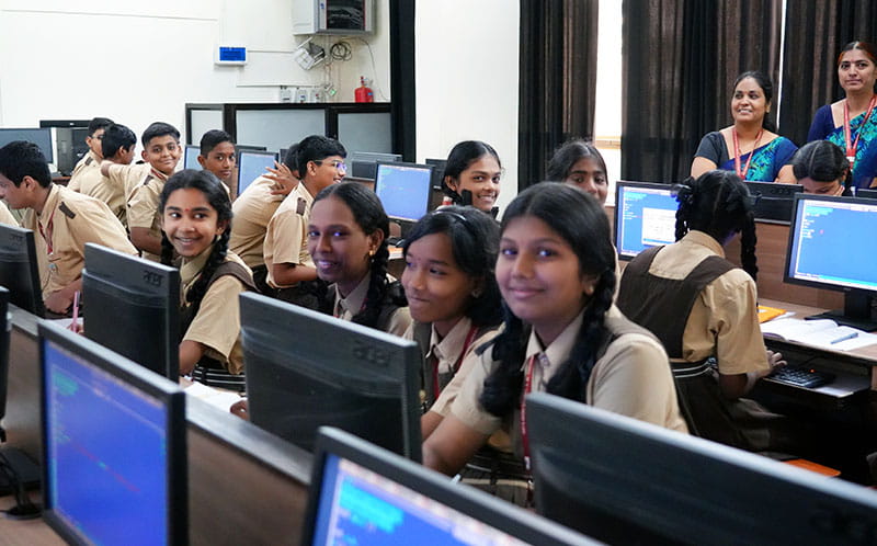 A group of students in a computer lab, smiling and engaging in a collaborative learning environment.