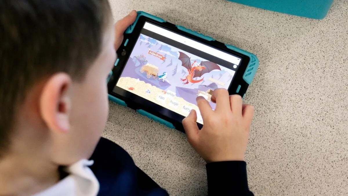 A young student engages with a Lumio educational software on a tablet, arranging adjectives to match with animated animals on the screen.