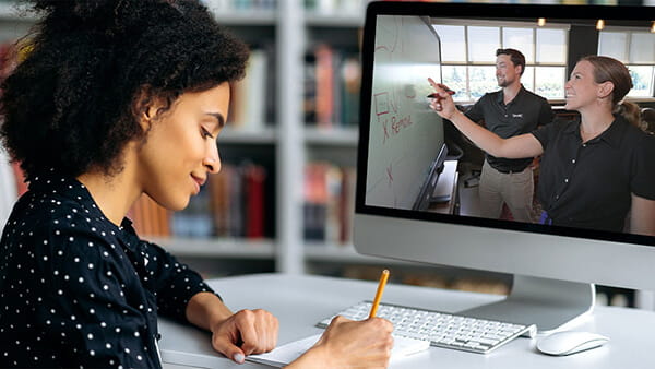 Virtual learning session with a woman observing a SMART Board product demonstration by business professionals while taking notes.